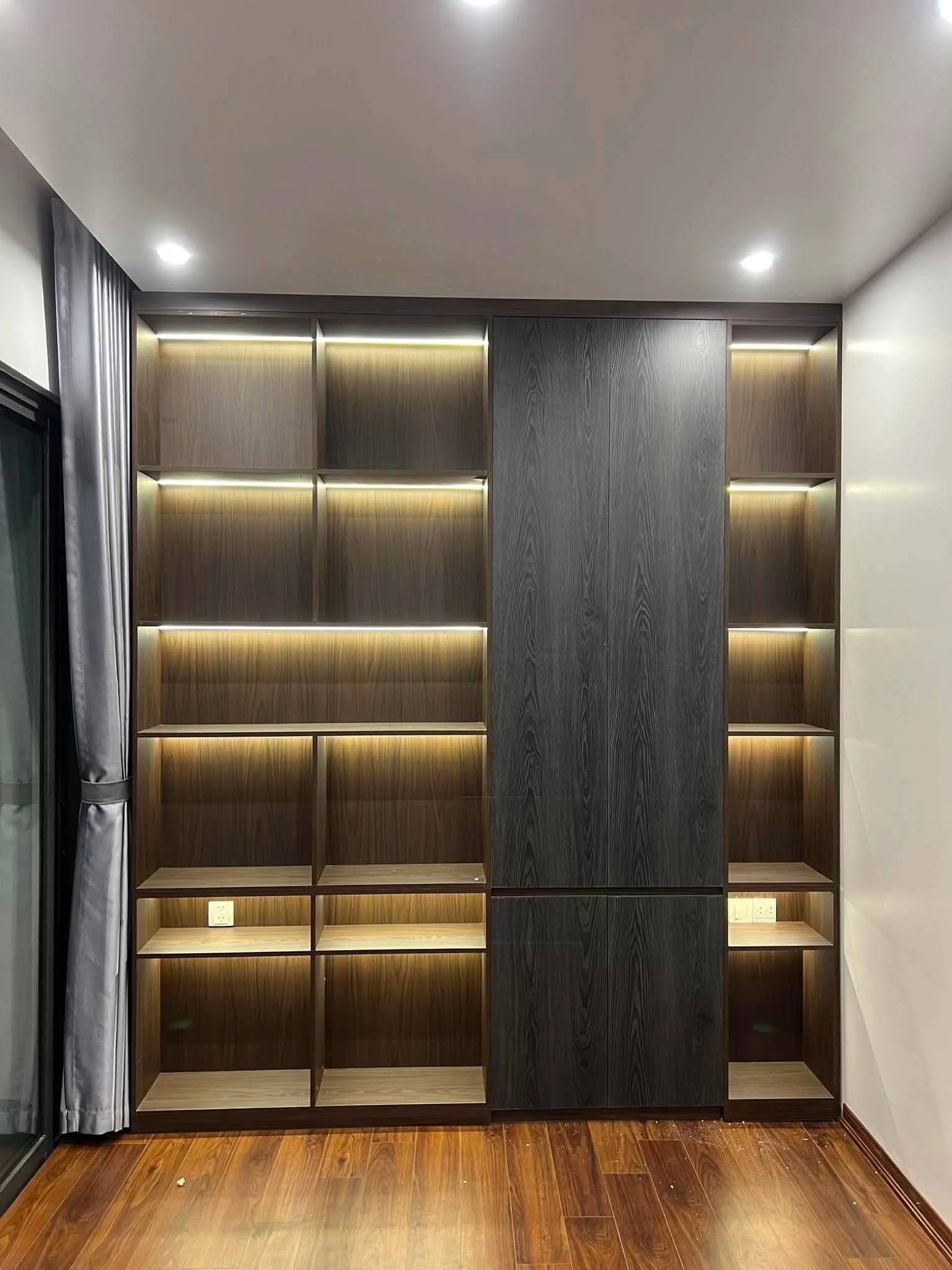 Hệ tủ gỗ màu tối cao sát trần với nhiều khoang trưng bày gắn đèn led