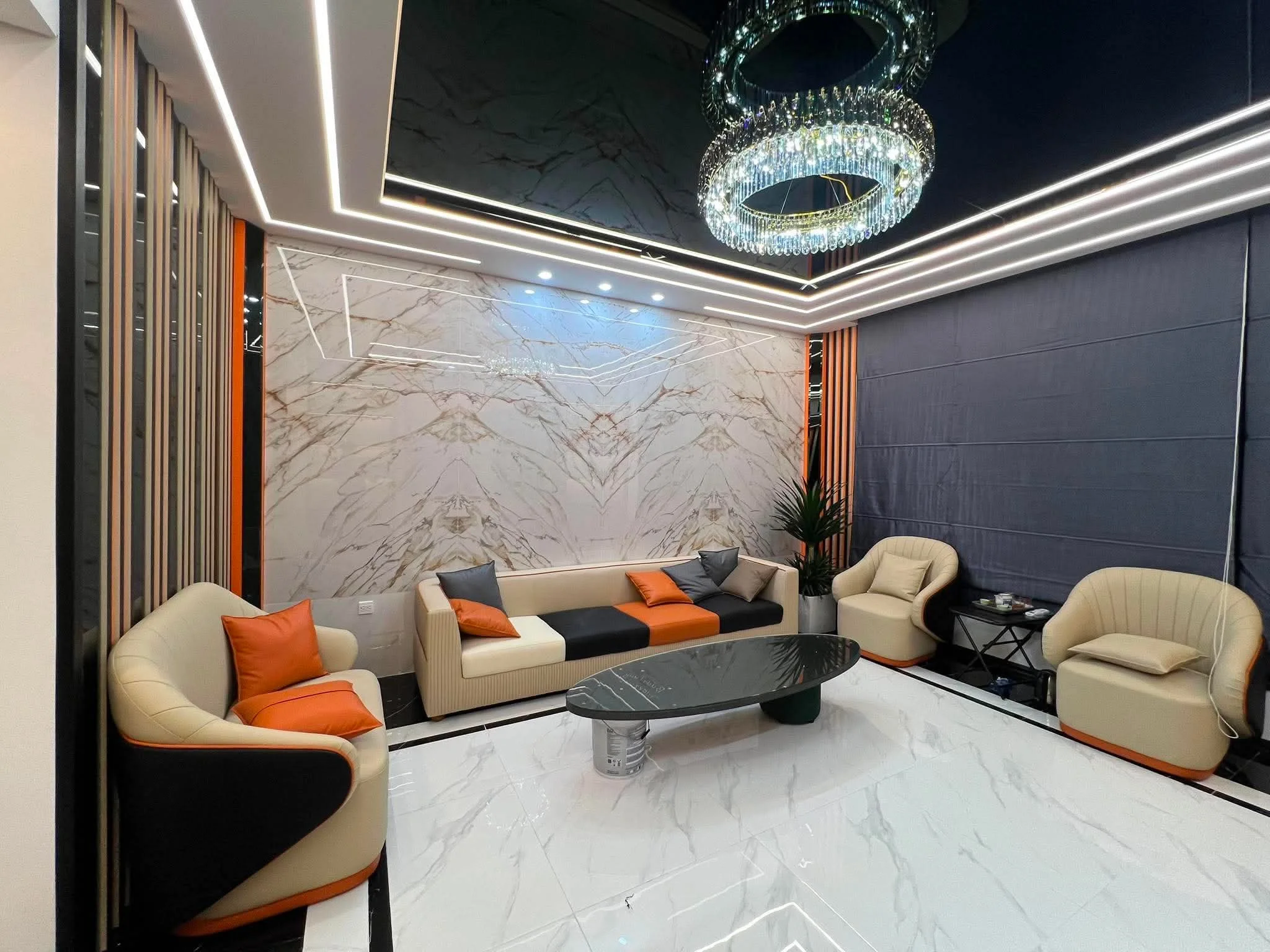 Phòng khách hoàn thiện với vách lớn, sofa màu kem đen và các điểm nhấn cam